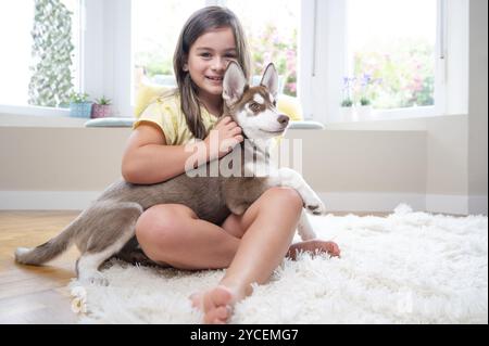 Lächelndes Mädchen und ihr sibirischer Husky-Welpe auf Teppich zu Hause. Stockfoto