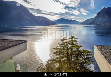 Sonniger Blick auf den Luganer See und gute Wohngebäude (im Vordergrund), ca. 5-6stöckiges Gebäude, am Ufer mit einer fantastischen Zedernholzanlage im Stockfoto
