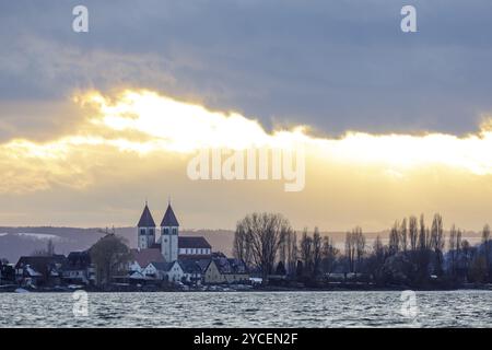 Kirche St. Peter und Paul und Häuser am See bei Sonnenuntergang, dramatische Wolken am Himmel, ruhige Wasserlandschaft, Hafen, Allensbach, Bodensee, Stockfoto