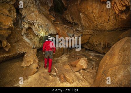 Ein Speläologe mit Helm und Scheinwerfer, der eine Höhle mit reichen Stalaktiten- und Stalagmitenformationen erforscht. Grafik Stockfoto