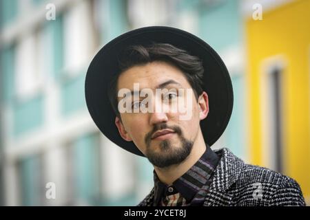 Porträt eines hübschen jungen Mannes mit einem Mantel im Freien. Ein ernster Mann mit Mantel, Hut und Hemd, der selbstbewusst in die Kamera blickt Stockfoto