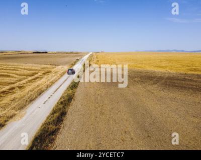 Aus der Vogelperspektive eines Autos, das im Sommer auf einer Landstraße zwischen Weizenfeldern fährt Stockfoto