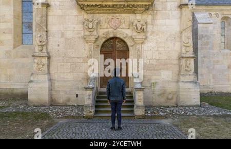 Ein junger Touristenmann, der vor einer schönen mittelalterlichen Chatedral-Tür steht. Ein Mann vor einer Eingangstür einer alten Architekturkirche in Alba IUL Stockfoto