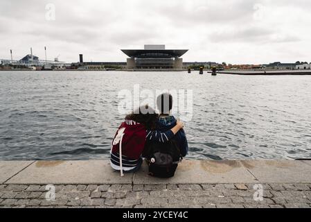 Ein paar der jungen Menschen umarmt sitzen an der Waterfront. Ansicht von hinten Stockfoto