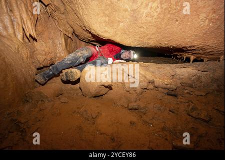 Ein Speläologe mit Helm und Scheinwerfer, der eine Höhle mit reichen Stalaktiten- und Stalagmitenformationen erforscht. Grafik Stockfoto