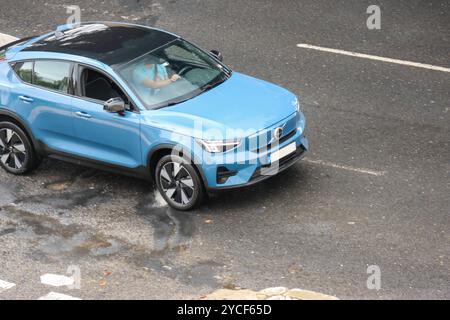 Der moderne volvo xc40 in Elektroblau lädt das Fahren auf nasser Straße nach dem Regen mit dem Fahrer hinter dem Lenkrad auf Stockfoto