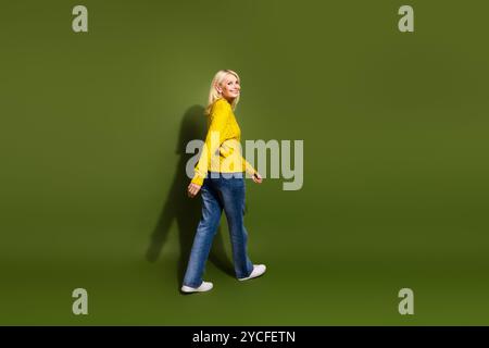Foto der schönen positiven Dame tragen trendigen gelben Pullover Spaziergang leeren Raum isoliert auf grünem Hintergrund Stockfoto