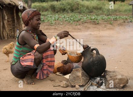 Frau aus der Banna-ethnischen Gruppe, die ein kaffeähnliches Getränk aus einem Tontopf in ein Trinkgefäß aus einem Kalabasch aus dem südlichen Omo-Tal in Äthiopien gießt Stockfoto