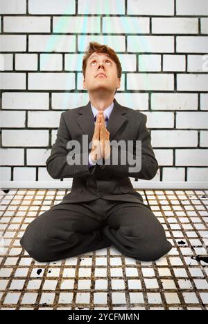 Komischer Geschäftsmann auf Knien betend Stockfoto