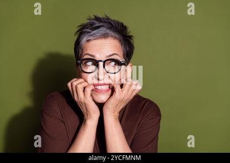 Foto-Porträt des grauen Haares schöne fröhliche Rentnergroßmutter in Brille beißende Nägel, die den leeren Raum nervös auf Khaki-Farbe aussahen Stockfoto
