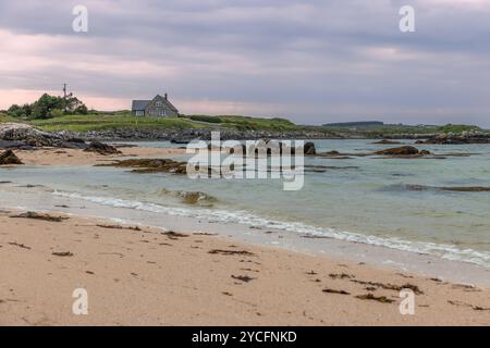 Gurteen Beach at Sunset bietet ein malerisches Steinhaus mit Blick auf eine ruhige Küste in Irland. Das sandige Ufer, gesäumt von Algen und Felsen, Stockfoto