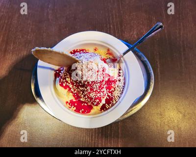 Vanilleeis mit roter Erdbeersauce und weißen Schokoladenstreuseln in einer Schüssel als Spaghetti-Eis mit einem runden Kegel serviert Stockfoto
