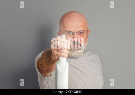 Ein bärtiger Mann in Brille hält die Sprühflasche, als würde er die Waffe auf die Kamera richten. Humorvolle Werbung Stockfoto