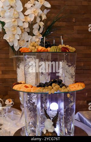 Elegantes dreistufiges Obst-Display mit Blumen und Kerzen. Stockfoto