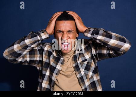 Foto-Porträt des netten jungen Mannes Berührungskopf Angry tragen trendiges kariertes Outfit isoliert auf dunkelblauem Hintergrund Stockfoto