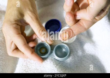 Alltagsroutine einer Person mit Kurzsichtigkeit: Eine Frau hält mit einer Hand einen Etui und mit der anderen eine weiche braune Kontaktlinse mit einem Irismuster, Nahaufnahme Stockfoto