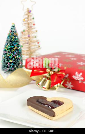 Eine Shortbread-Marmelade gefüllt mit Schokoladenherz auf einem Teller unter weihnachtlichen Dingen. Der Fokus liegt nur auf dem Shortbread Biscuit. Stockfoto