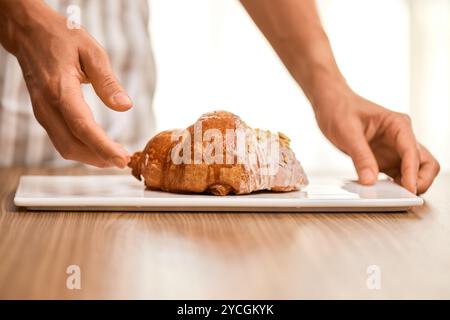 Weibliche Hand, die frisches, handgemachtes Croissant auf weißem Teller hält Stockfoto
