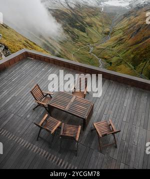 Holzstühle und Tisch auf der Terrasse in den Bergen. Esstisch mit Aussicht, Alpen im Hintergrund. Stockfoto