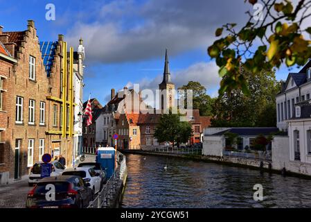 Backsteinbauten säumen den Kanal Sint Annarei und den Turm der Sint Annkerk aus dem 17. Jahrhundert von Molenbrug aka Mühlbrücke in Brügge, Belgien. Stockfoto