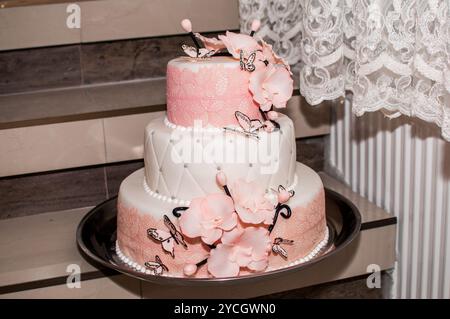 Eleganter dreistufiger Hochzeitstorte mit rosafarbenen Blumen und Schmetterlingen. Stockfoto