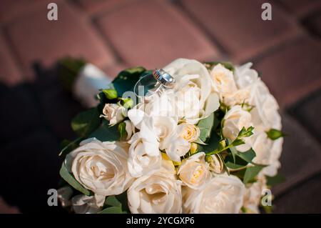 Eleganter Brautstrauß mit Hochzeitsringen und zarten weißen Rosen. Stockfoto