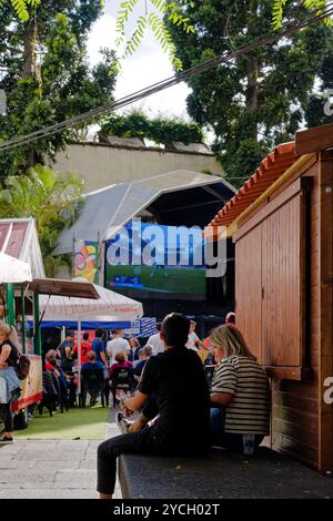 Paare in Funchal sehen ein Live-Fußballspiel auf einer großen Außenleinwand, entspannte Atmosphäre inmitten von Imbissständen und schattigen Bäumen Stockfoto