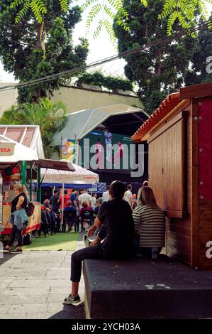 Paare in Funchal sehen ein Live-Fußballspiel auf einer großen Außenleinwand, entspannte Atmosphäre inmitten von Imbissständen und schattigen Bäumen Stockfoto