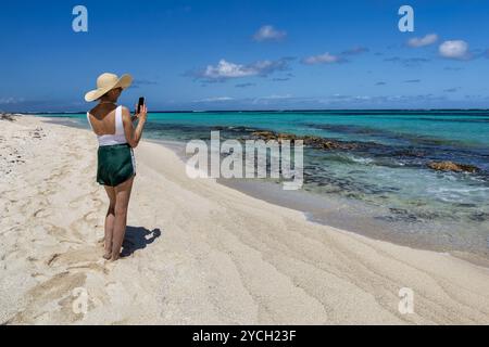 Eine Frau, die mit ihrem Handy ein Foto vom Wasser entlang des Shoal Bay Beach auf der Insel Anguilla macht. Stockfoto