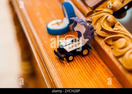 Charmante Spielzeugauto-Schmuckschatulle mit Kreuzring auf Holzoberfläche. Stockfoto