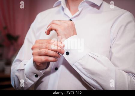 Elegante Manschettenknöpfe mit verstellbarem Mann auf einem knusprigen weißen Hemd in einer stilvollen Umgebung. Stockfoto