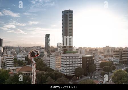 Die Sonne untergeht über einem modernen Stadtbild mit hohen Gebäuden, einem Vergnügungspark und Bäumen Stockfoto