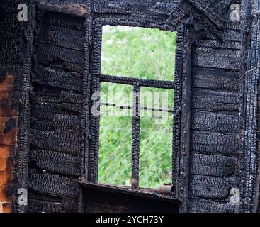 Verbranntes Holzfenster mit Blick auf grüne Bäume Stockfoto