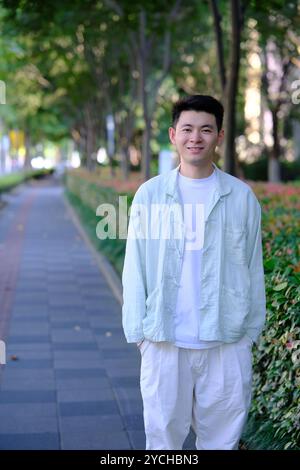 Lächelnder chinesischer junger Mann draußen, der in die Kamera schaut Stockfoto