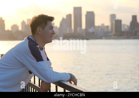 Seitenansicht eines lächelnden asiatischen jungen Mannes in der Abenddämmerung Stockfoto