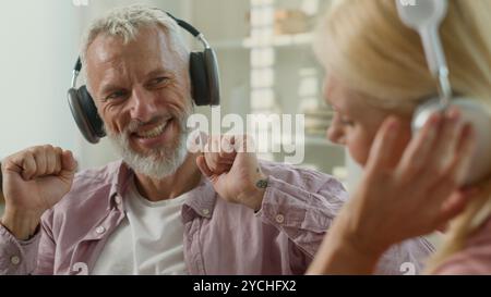 Glückliche sorglose kaukasische Familie Paar Mann Frau 60er Großmutter Großvater Rentner hören Musik mit Kopfhörern tanzen zu Hause hören hören hören Stockfoto
