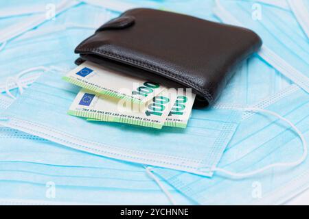 Schwarze Herren Brieftasche mit Euro Geld innen auf den blauen Einweg-medizinischen Gesichtsmasken. Handel mit medizinischen Masken. Unternehmen während einer Pandemie oder Epidemie Stockfoto