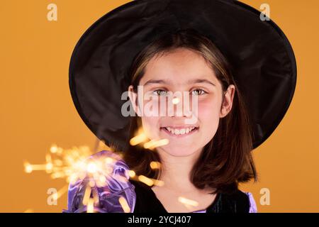 Konzentriere dich auf das Gesicht eines glücklichen Jugendlichen Mädchens in Halloween Hexenkostüm und Hut, der brennenden Glitzer vor der Kamera hält Stockfoto