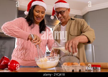 Weihnachten, weihnachtsmütze tragen, multirassisches Seniorenpaar backen für den Urlaub, zu Hause Stockfoto