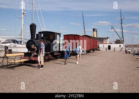 HJO, SCHWEDEN AM 15. MAI. Blick auf einen alten Zug und ein Dampfschiff im Hintergrund am 15. Mai 2024 in Hjo, Schweden. Nicht identifizierte Menschen im Hafen. Edito Stockfoto