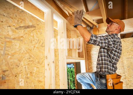 Ein erfahrener Zimmermann arbeitet fleißig daran, während der Tageslichtstunden Holzbalken in einem Bauprojekt zu installieren, um die strukturelle Integrität zu gewährleisten. Stockfoto