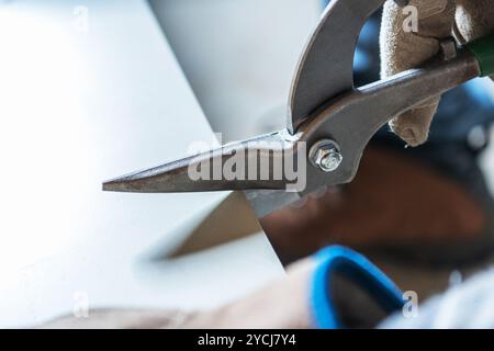 Ein Arbeiter schneidet vorsichtig eine dicke Materialplatte mit einer schweren Schere ab, während er in einer Werkstatt Schutzhandschuhe trägt. Stockfoto