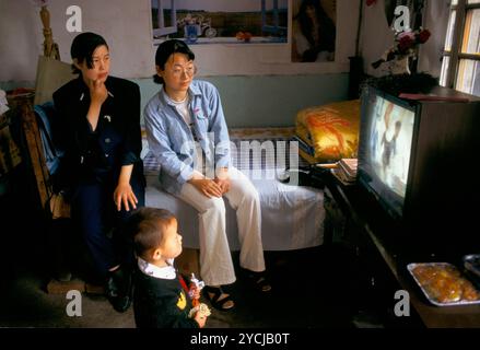 China 1990er Jahre Chinesische Familie Teenager im Familienhaus Liufu Dorf Provinz Anhui Fernsehen. 1998 ländliche Gemeinschaft Familienleben. Dies ist das Wohnzimmer und Schlafzimmer und wo die Gäste hingebracht werden. Es gab mehrere Fernseher in diesem kleinen Familienhaus. Der Vater war Getreidehändler, hatte aber fast nichts zu verkaufen. Die Mutter hatte sich von der Familie getrennt und lebte in einem anderen Haus im Dorf. Sie war Schullehrerin. Es gab vier Töchter, von denen zwei Englisch sprachen. Es gab keine Toilette oder ein Bad und das alles wurde hinter einem Bildschirm im Garten gemacht. Ich würde sagen, dass sie Stockfoto