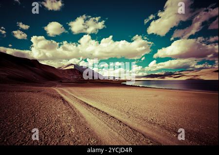 Leere Landstraße, die durch Wüstenprärie unter bewölktem Sonnenuntergangshimmel in der Nähe des TSO Moriri Lake führt. Himalaya-Gebirgslandschaft. Indien, Stockfoto