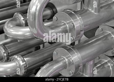 Viele glänzende, gebogene Edelstahlrohre des Kühlsystems für Industrieanlagen. Abstrakter industrieller Hintergrund. Stockfoto