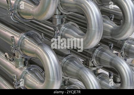 Viele glänzende, gebogene Edelstahlrohre des Kühlsystems für Industrieanlagen. Abstrakter industrieller Hintergrund. Stockfoto