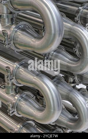 Viele glänzende, gebogene Edelstahlrohre des Kühlsystems für Industrieanlagen. Abstrakter industrieller Hintergrund. Stockfoto