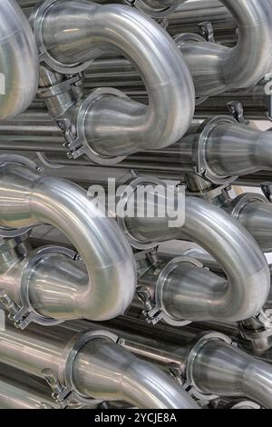 Viele glänzende, gebogene Edelstahlrohre des Kühlsystems für Industrieanlagen. Abstrakter industrieller Hintergrund. Stockfoto