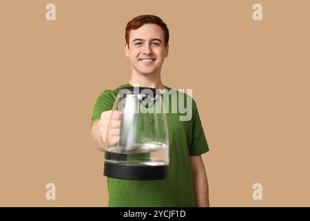 Schöner junger Mann mit modernem Wasserkocher auf beigefarbenem Hintergrund Stockfoto