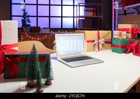 Laptop mit leerem Bildschirm und Weihnachtsgeschenkboxen auf dem Tisch im Postamt Stockfoto